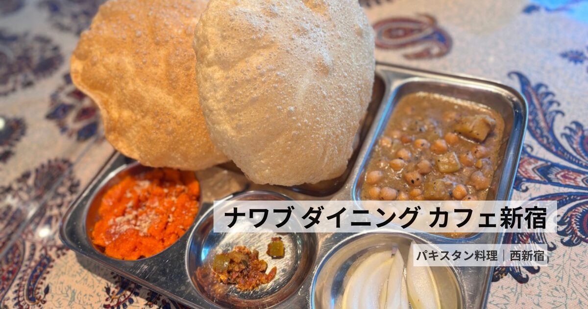 ナワブ新宿で提供される南アジアの朝食「ナシタ」。揚げたてのプーリー、ヒヨコ豆のカレー、甘いハルワなどが写ったトレイと共に、タイトル「南アジアのナシタ？とフィッシュカレーの小さな旅」が重ねられている。背景には伝統的な模様のテーブルクロスも見える。