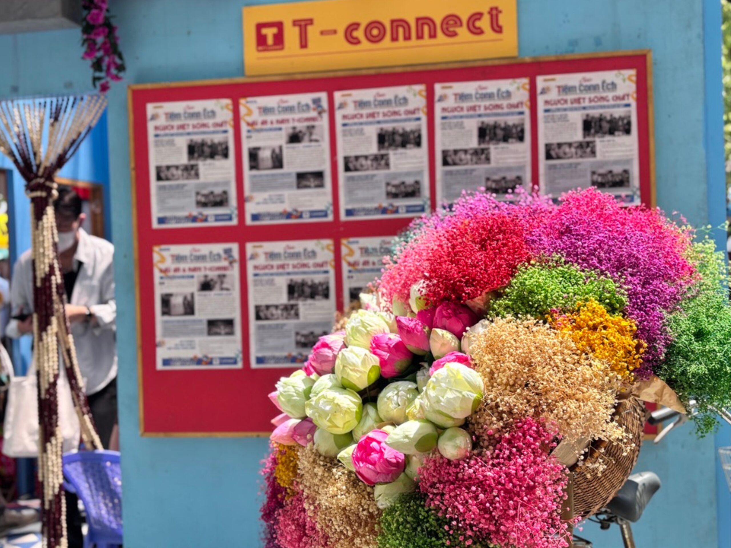 ベトナムフェスティバルのT-connectブース前に展示されたカラフルな花束。背景にはベトナム語のポスターが掲示され、観光案内や文化イベントの情報が並ぶ。