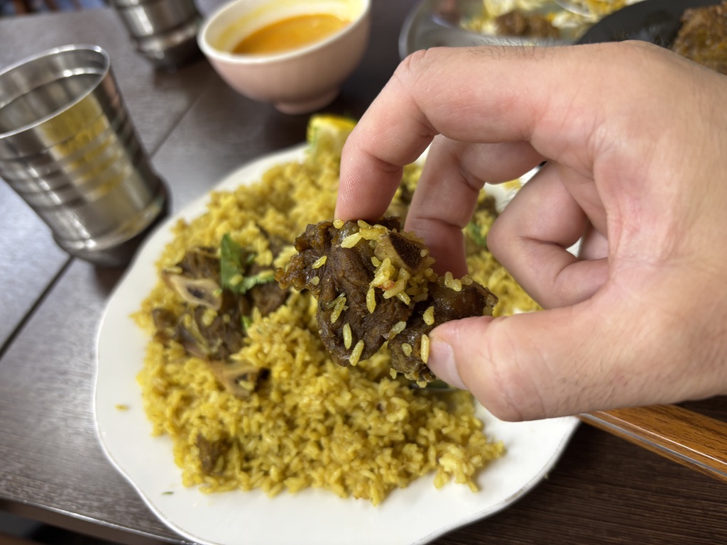 「骨付きビーフとスパイスライスを手で食べるビーフテハリの一口シーン。現地式の食べ方。」