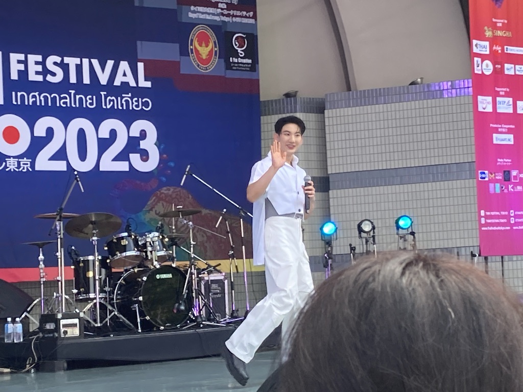 「タイフェスティバル2023」のステージに登場したジラキット・クーアリヤクンさん来日。観客に手を振る様子。背景にはドラムセットとイベントバナーが見える。2gether