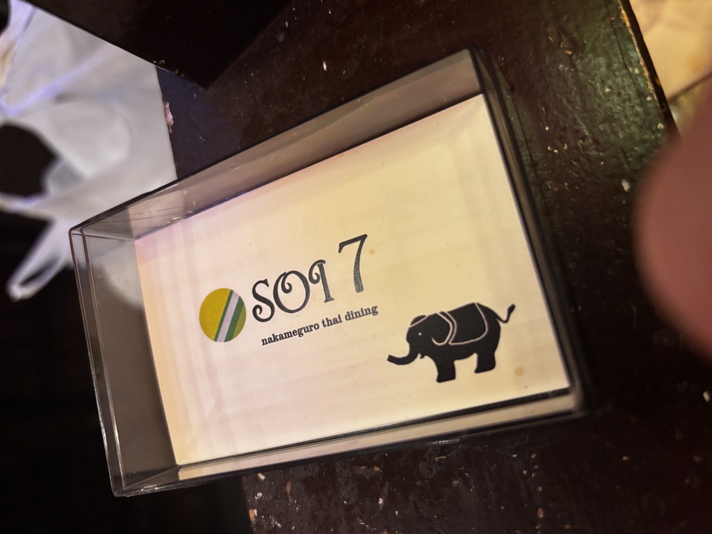 「中目黒のタイ料理店『Soi7』の店名カード。白い背景に緑と黄色の円形ロゴ、象のシルエットが描かれた可愛らしいデザイン」