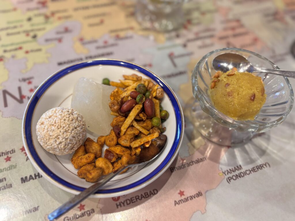 南インドの地図の上に置かれた白いPetha、Til Ladoo、ナムキンのプレート。異国情緒ある背景と鮮やかなインド菓子が特徴。