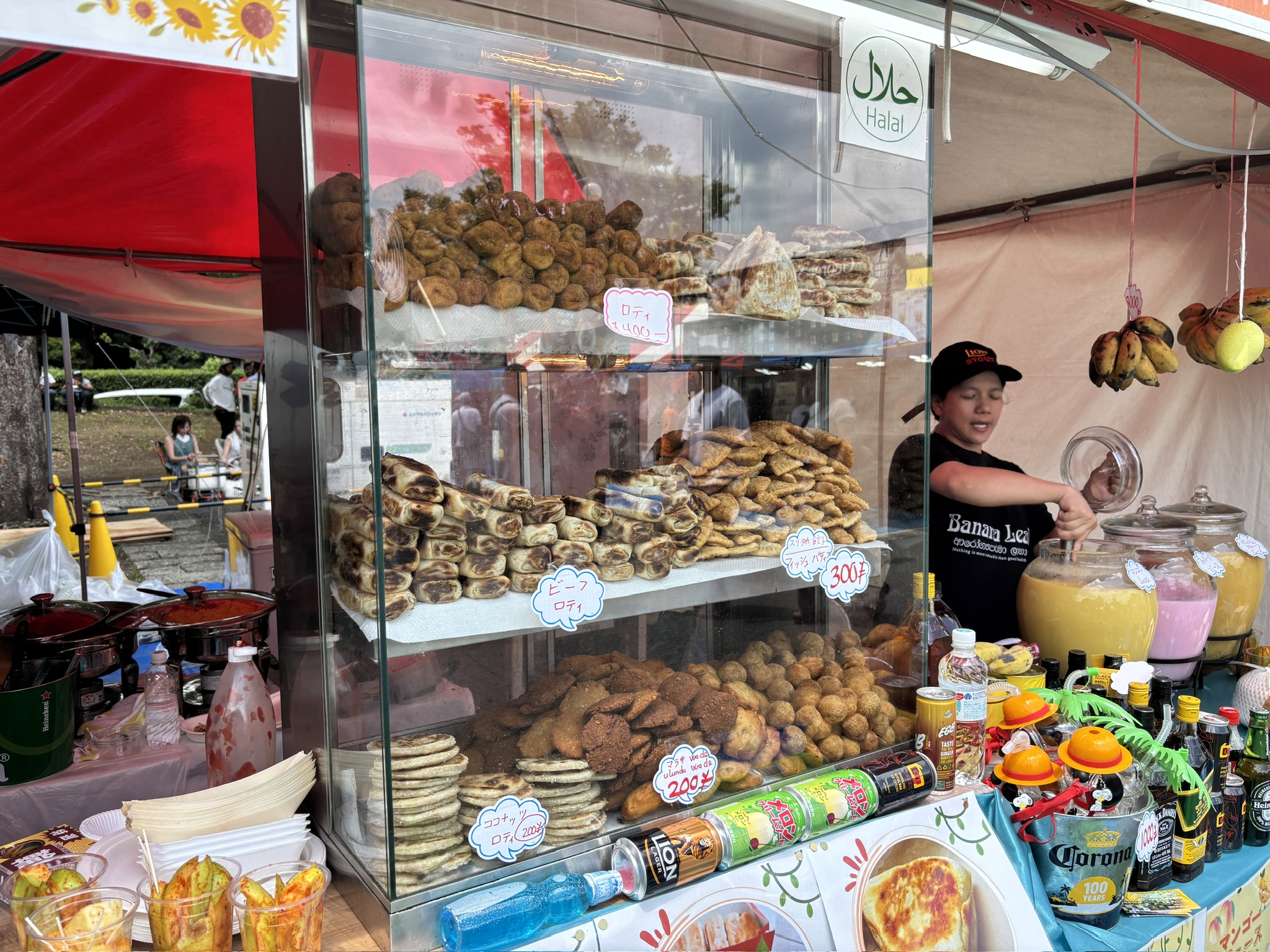 スリランカフェスティバルの屋台。左はショーケースに並ぶサモサや揚げ菓子などの軽食、右はカレーや炒め物が並ぶ鍋から料理を盛り付けるスタッフの様子。
