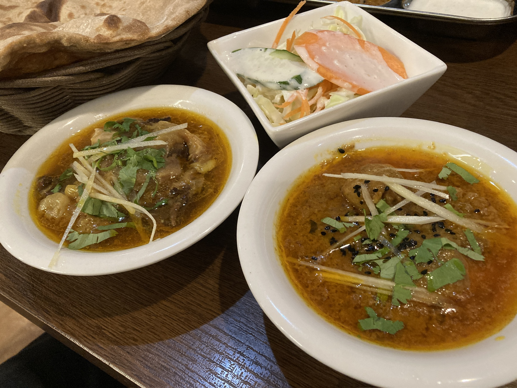 「黄金色のグレービーに鶏肉が沈むチキンアチャーリーカレー。黒いマスタードシードが浮かび、細切りショウガと香菜が彩りを添えている」