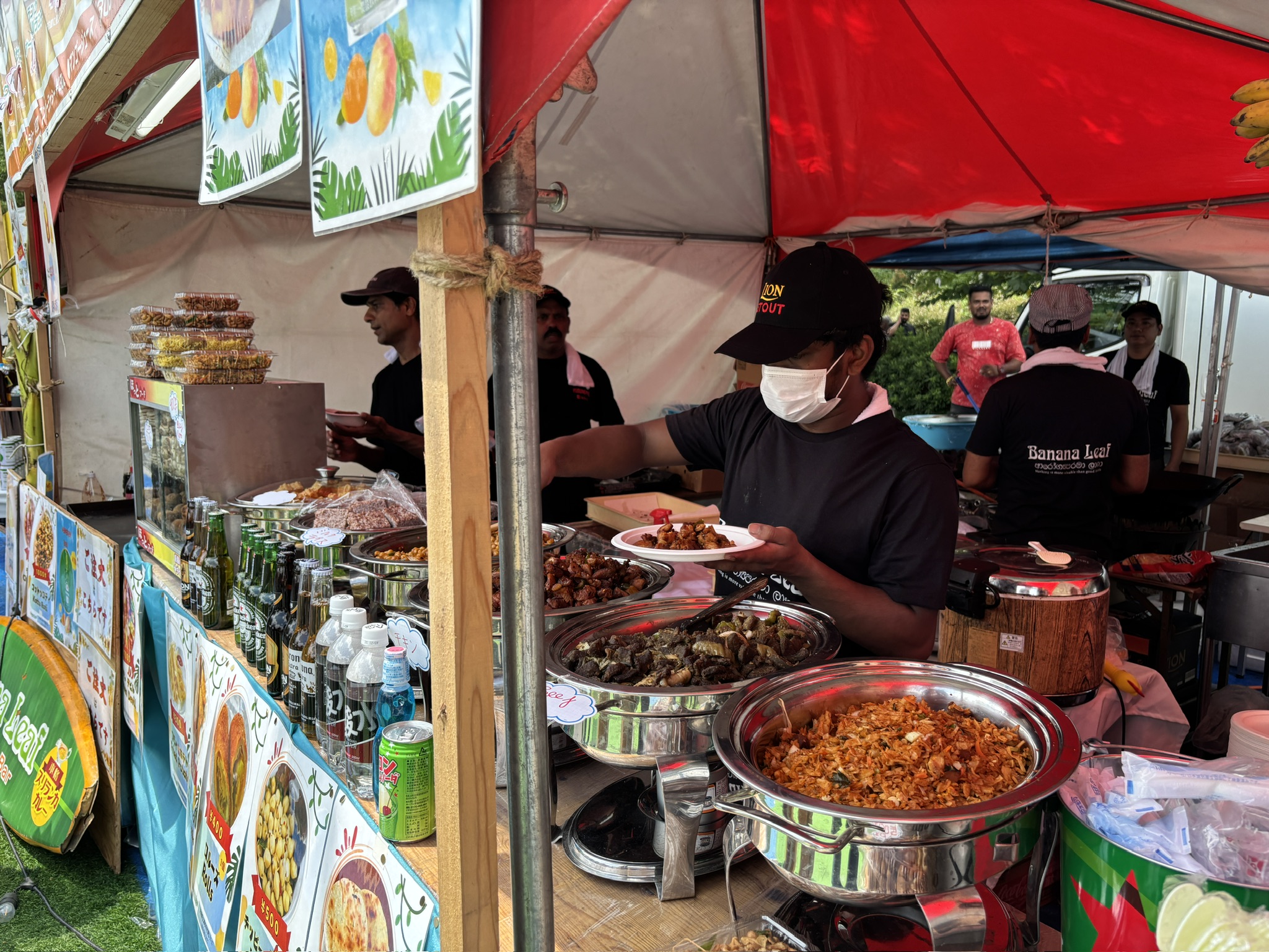 スリランカ料理屋台で、スタッフが大鍋からカレーや炒め物を皿に盛り付けている様子。