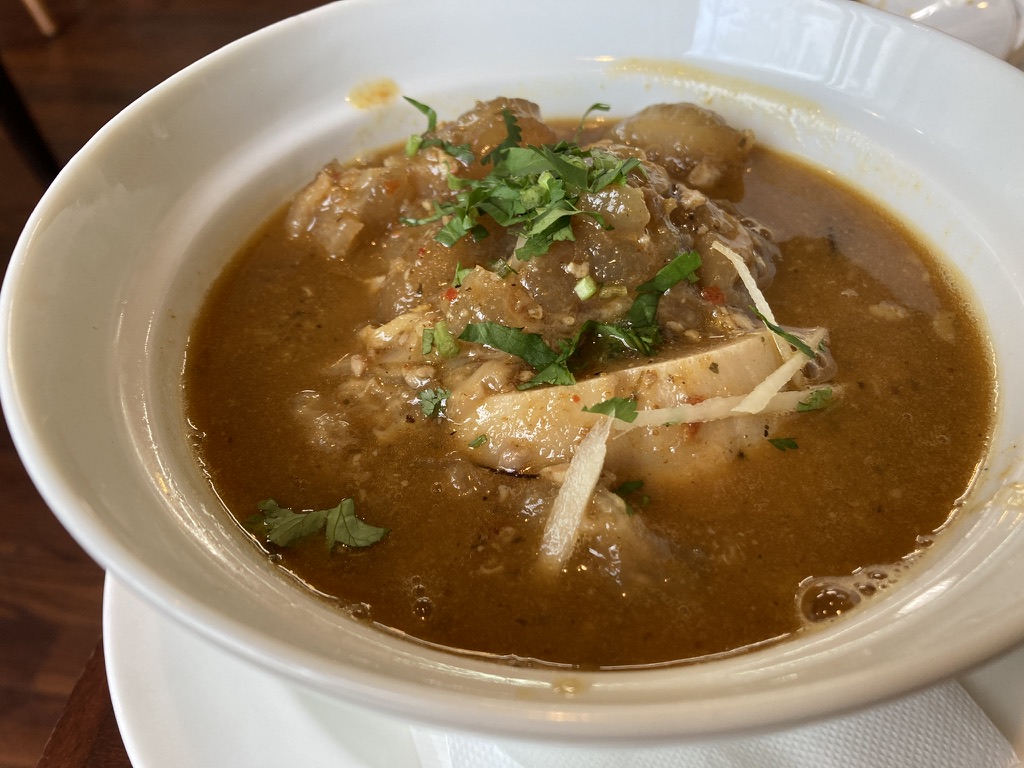 「深い茶色のスープに牛のすね肉と蹄が煮込まれたビーフパヤ。骨や腱から溶け出したゼラチンでとろみがあり、上には細切りショウガと刻み香菜がトッピングされている」