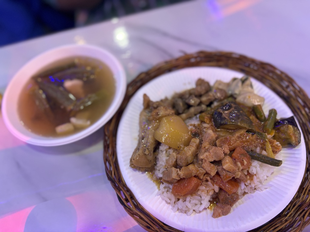 ご飯の上に盛られたフィリピン定番料理アドボなどと、酸味のあるスープ（シニガン）。家庭的な見た目。