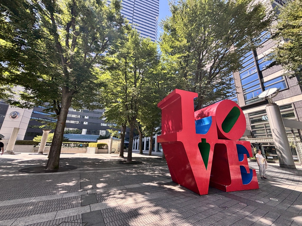 新宿アイランド前にある有名な赤い「LOVE」モニュメントと、木陰の広がる都会の景色。