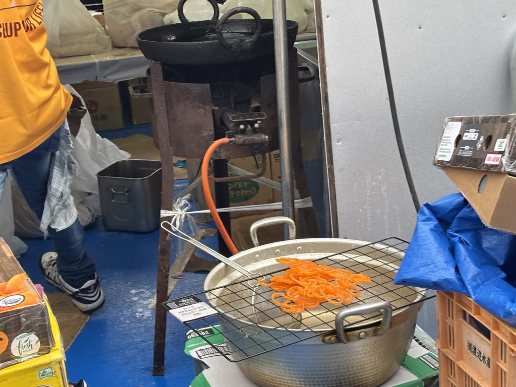 揚げたてジャレビが並ぶ鍋と屋台の様子
Freshly fried Jalebi sweets at the festival stall.