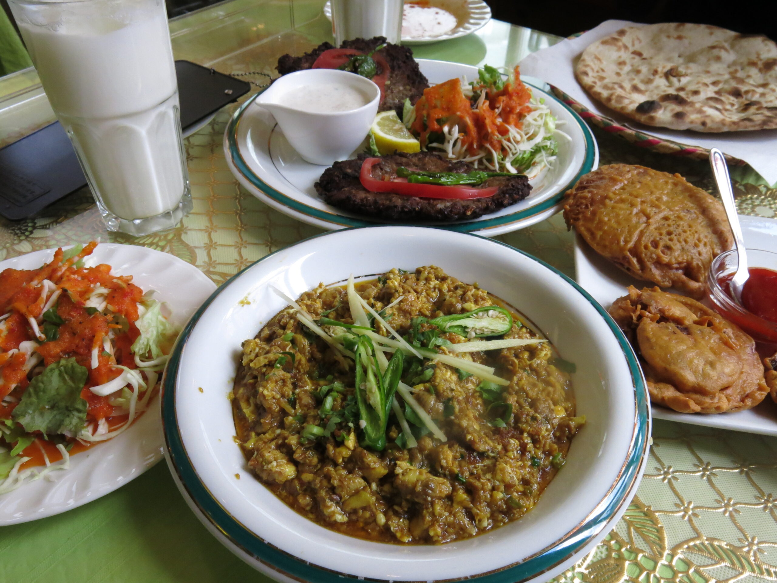 羊の脳みそをスパイスと香味野菜で炒めたパキスタン料理マガジフライ(Maghaz Fry)。濃厚でまろやかな旨味が特徴の一皿と、サラダ、チャパティ、揚げ物、ラッシーなどのセット料理。