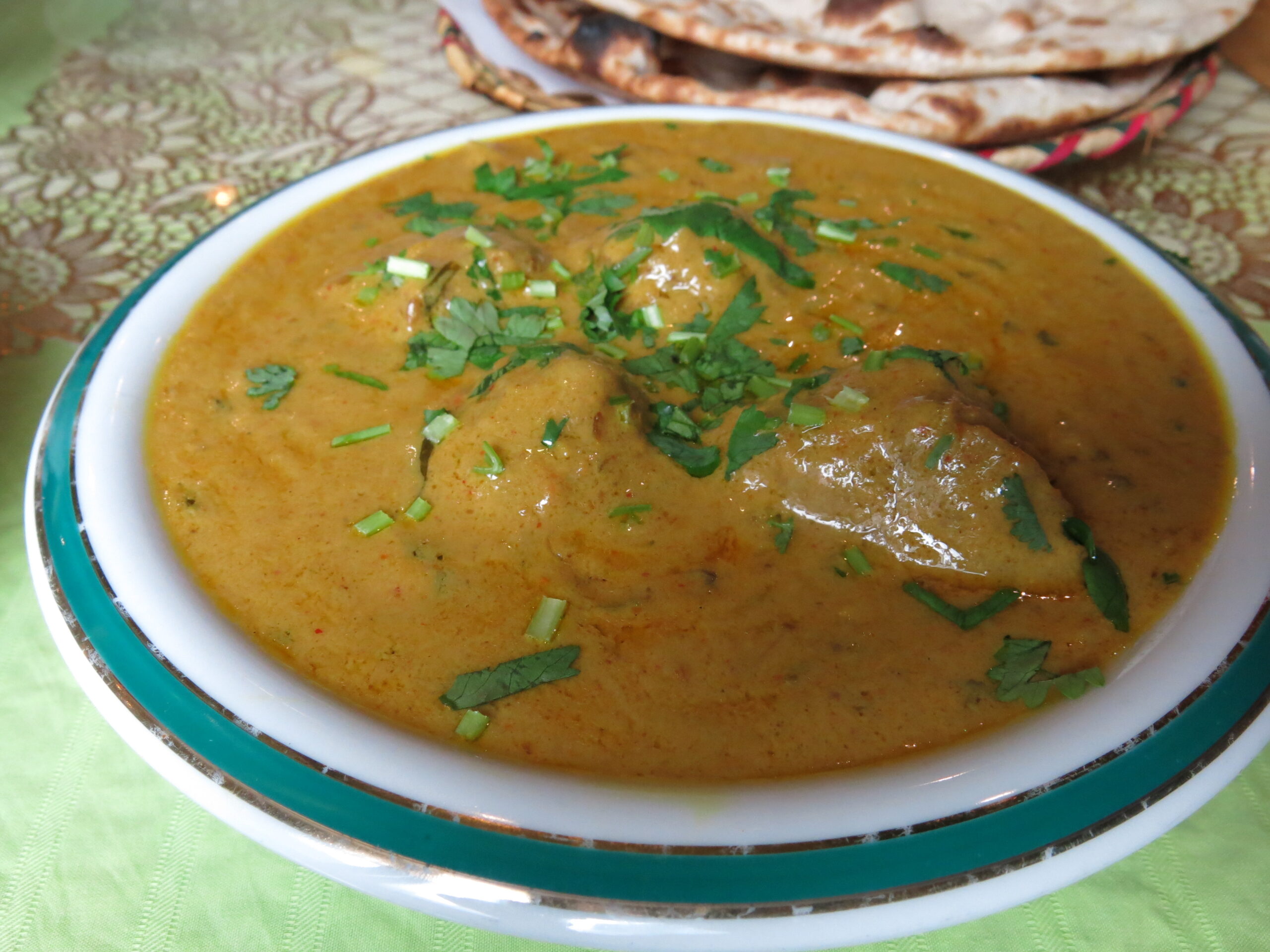「縁に緑のラインが入った白い器に盛られた濃い黄色のカレー。中にはベサン粉の団子が入り、上から刻みパクチーがたっぷりと散らされている」