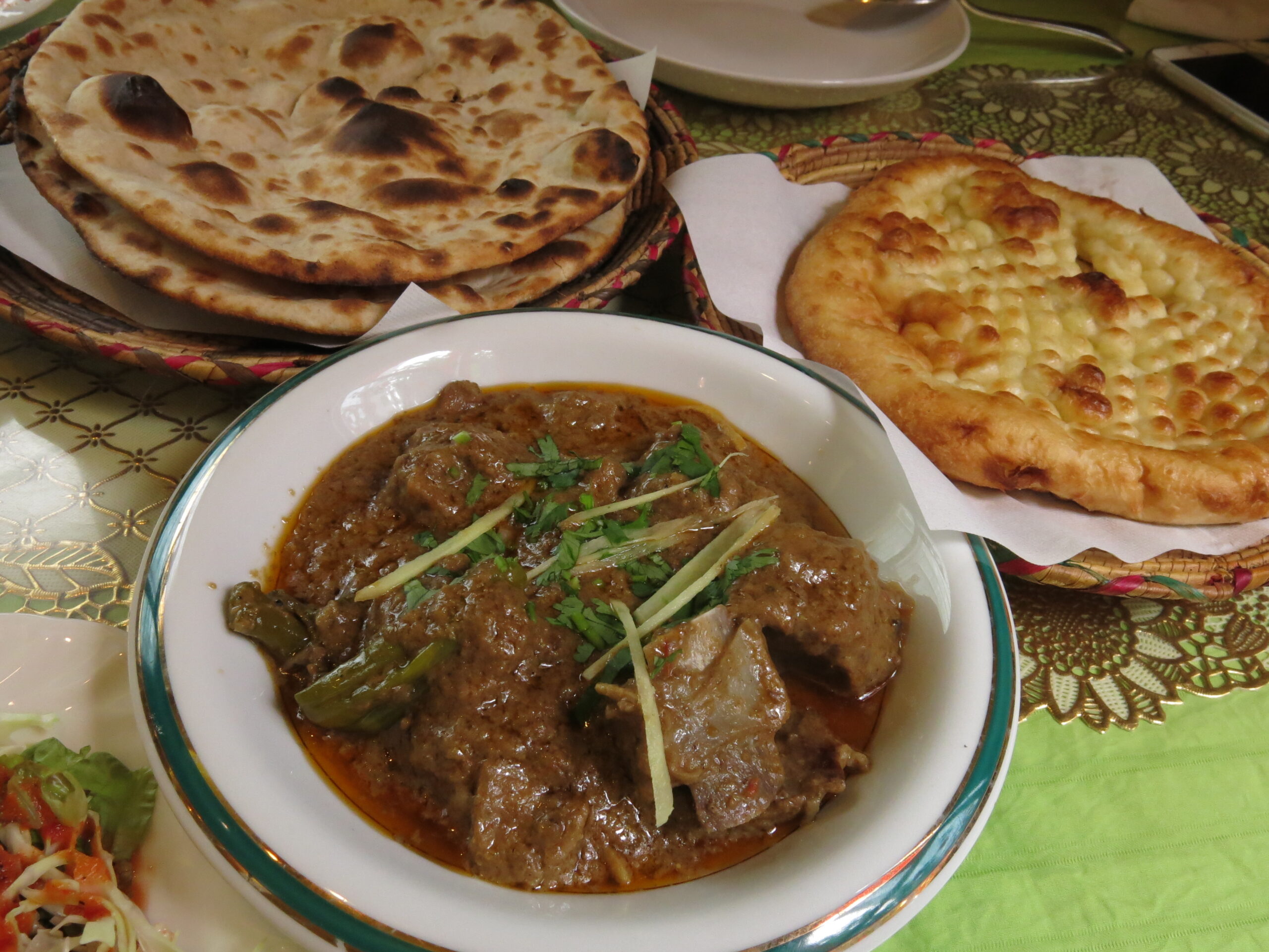 「淡い色合いのホワイトアチャーリーカレー。骨付き肉の上に細切りショウガと香菜がのり、奥には香ばしく焼かれたナンとふっくらしたカブリナンが並ぶ」
