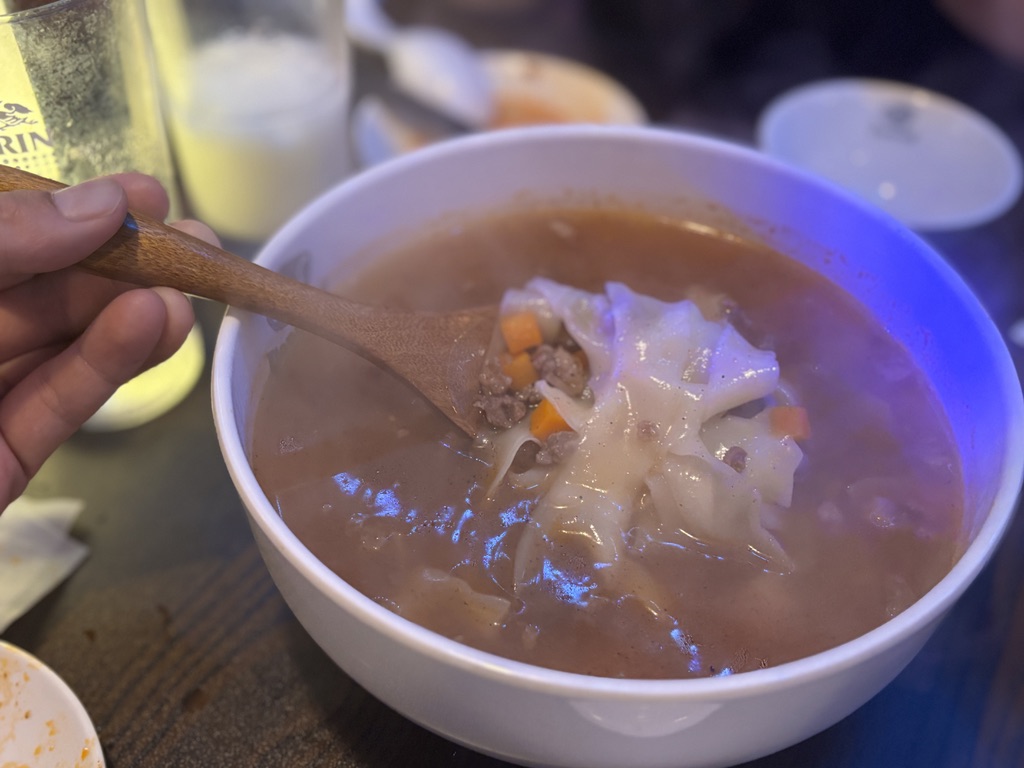 ウイグルの平打ち麺入りスープ「ナラン麺 」。スプーンで持ち上げられた幅広麺とひき肉、野菜がスープに浮かぶ