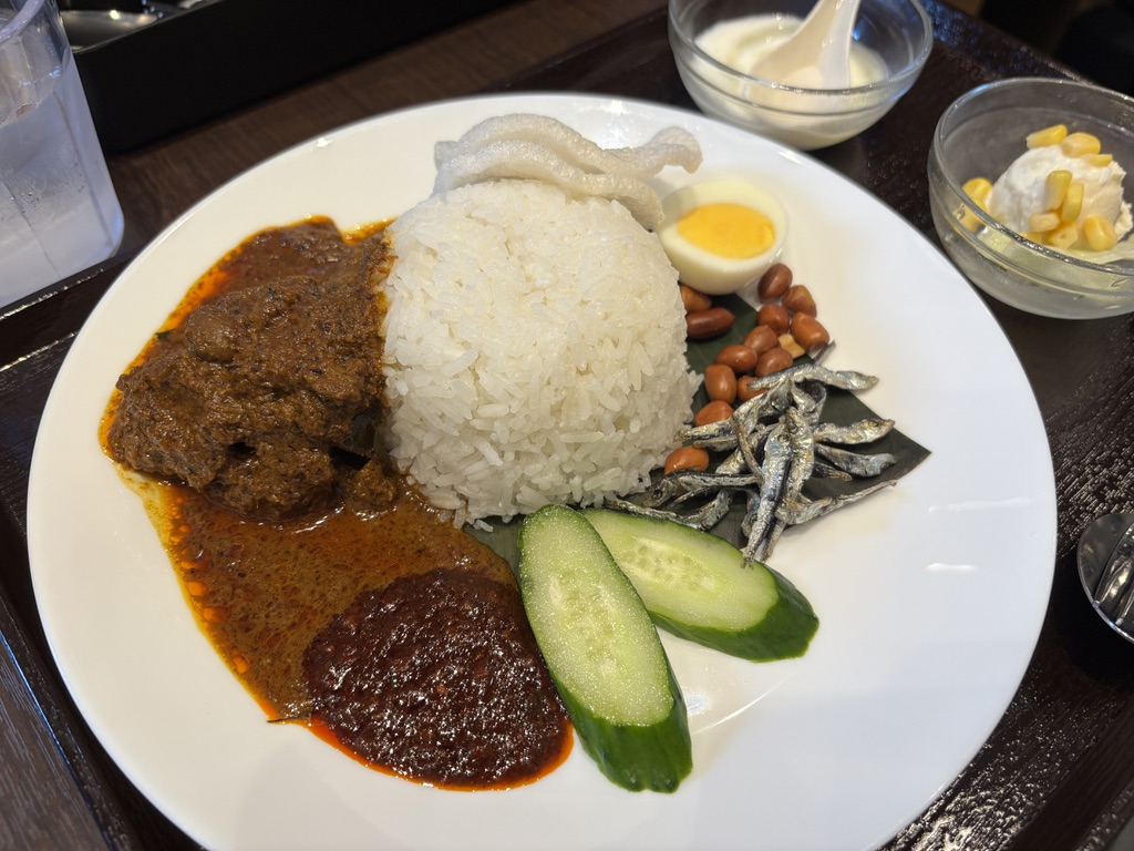ナシレマッのプレート。ご飯を中心にチキンレンダン、煮卵、揚げ煎餅、じゃこ、きゅうり、ピーナッツ、サンバルが彩りよく盛り付けられている。