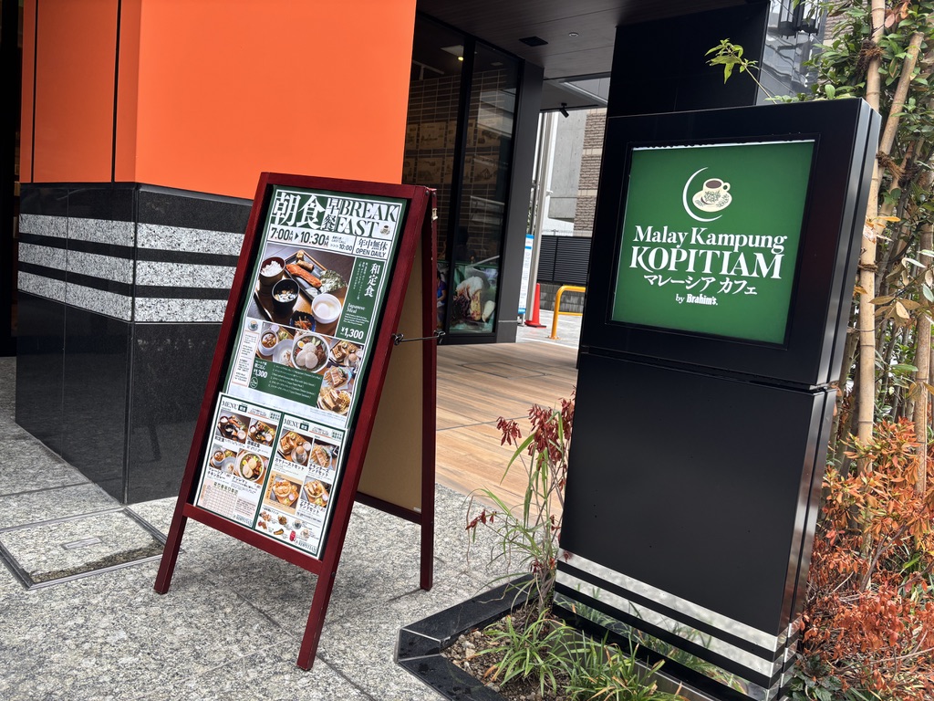 「マレーカンポン コピティアム水道橋店」の外観と緑色の看板。店頭には朝食メニューの立て看板が設置されている。
