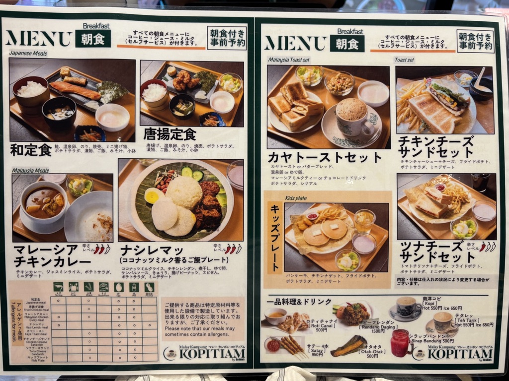 「マレーカンポン コピティアム水道橋店」の朝食メニュー看板。和定食、唐揚定食、マレーシアチキンカレー、ナシレマッ、カヤトーストセット、チキンチーズサンドセット、ツナチーズサンドセット、キッズプレートなどが写真付きで紹介されており、ドリンクや単品メニューも記載されている。全品ドリンクバー付き（セルフサービス）の案内あり。